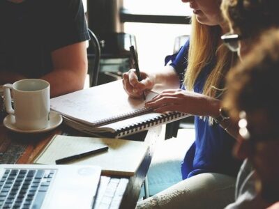 Pessoas reunidas em uma mesa utilizando notebook e celular