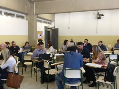 sala de aula com professores sentados nas carteiras conversando em grupos