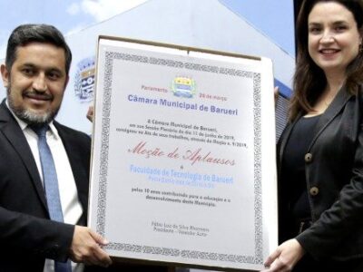 mulher e homem seguram a placa de homenagem